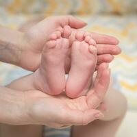 de la mère mains tenir le de bébé jambes. le le tout-petit pieds sont dans celui de maman palmiers. photo