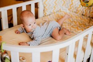 le bébé mensonges dans une lit de bébé sur le sien ventre. photo