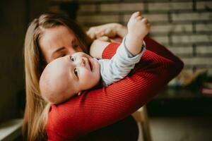 une mère détient une bébé dans sa bras. une maman baisers une nourrisson. une femmes câlins sa tout-petit. une fille a amusement et se réjouit avec le enfant. photo