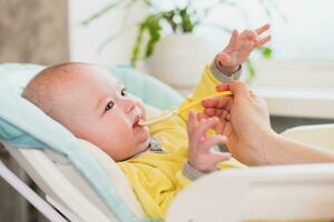 maman alimente le bébé. le mère met une cuillère de en purée dans le enfant bouche. le bambin mange aliments. photo