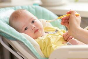 maman alimente le bébé. le bambin refuse à manger. le bébé ne fait pas vouloir à nutrition. le enfant tourné une façon de le nourriture cuillère. photo