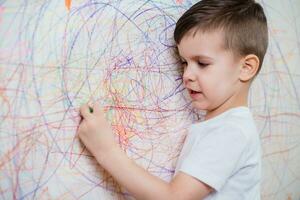 garçon dessine sur le mur avec coloré craie. le enfant est engagé dans la créativité à Accueil photo