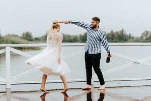 magnifique juste marié Danse pieds nus et avoir amusement sur le jetée par le l'eau. photo