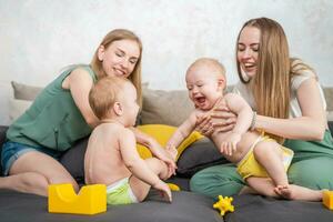 deux Jeune les mères sont en jouant avec leur content des gamins dans le pièce sur le canapé photo