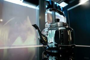 corbeau d'eau en acier inoxydable ou théière vintage sur cuisinière électronique sur fond bleu foncé moderne. photo