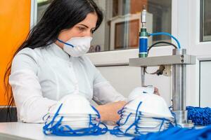 une femme travaux à une machine pour le fabrication de médical masques avec nanofibre et souder boucles à leur avec ultrason. coronovirus et covid-19 la prévention photo