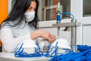 une femme travaux à une machine pour le fabrication de médical masques avec nanofibre et souder boucles à leur avec ultrason. coronovirus et covid-19 la prévention photo