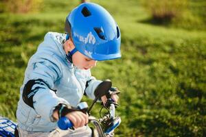 une enfant dans une casque monte une vélo sur une ensoleillé journée photo