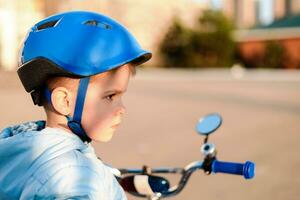 une enfant dans une casque apprend à balade une bicyclette sur une ensoleillé journée à le coucher du soleil photo