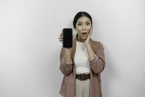 sous le choc Jeune asiatique femme employé portant cardigan est montrant copie espace sur sa téléphone filtrer, isolé par blanc Contexte photo