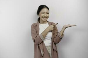 excité asiatique femme employé portant cardigan montrer du doigt à le copie espace à côté de son, isolé par blanc Contexte photo