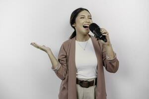 insouciant asiatique femme est ayant amusement karaoké, en chantant dans microphone tandis que permanent plus de blanc Contexte photo
