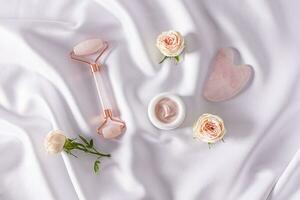 ensemble de produits de beauté et outils sur blanc satin Contexte avec vivre boutons de rose. Haut voir. cosmétique massage. Accueil se soucier. photo
