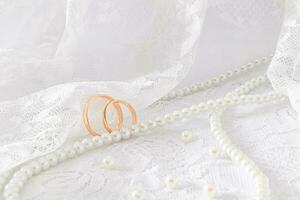 deux or mariage anneaux contre le doux plis de le dentelle en tissu de le de la mariée robe. une longue chaîne de perle perles. disposition pour conception. photo