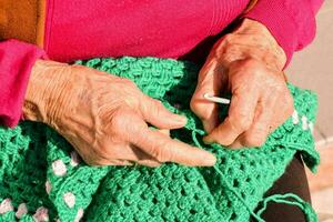 un personnes âgées femme est tricot une vert crocheté sac photo