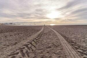 une paire de des pistes dans le le sable à le coucher du soleil photo