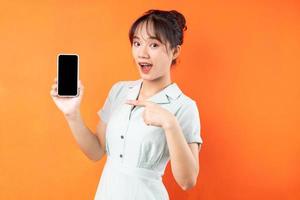 Portrait de jeune fille montrant l'écran du téléphone, isolé sur fond orange photo