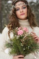 magnifique la mariée dans une blanc robe avec une bouquet dans une couvert de neige hiver forêt. portrait de le la mariée dans la nature. photo