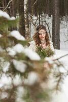 magnifique la mariée dans une blanc robe avec une bouquet dans une couvert de neige hiver forêt. portrait de le la mariée dans la nature. photo