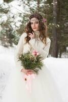 magnifique la mariée dans une blanc robe avec une bouquet dans une couvert de neige hiver forêt. portrait de le la mariée dans la nature photo