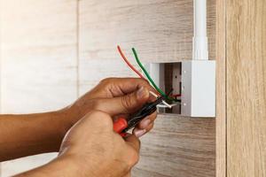 un électricien dénude les fils électriques dans une boîte en plastique sur un mur en bois pour installer la prise électrique. photo