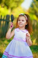 magnifique fille avec longue cheveux peigné chevelure. une enfant en portant une peigne pour le cheveux. bien enfant des promenades dans le tribunaux contre le Contexte de le clôture. photo