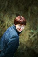 magnifique femme avec court cheveux regards dans le Cadre. portrait de une trentenaire femme. une fille dans une stable dans le Contexte de meules de foin. photo