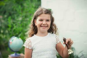 portrait de une mignonne brunette souriant et sonnerie une or école cloche en plein air sur une parc Contexte. retour à école. début ou fin de école an. photo