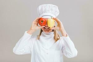 de bonne humeur femelle chef est ayant amusement avec des légumes sur gris Contexte. photo