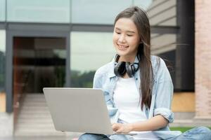 belle femme asiatique étudiante excitée vérifiant les résultats des tests de langue sur ordinateur portable. sourire fille heureuse étude en ligne. réserver sur le campus universitaire. portrait féminin sur l'université internationale d'asie. photo