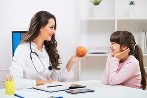 portrait de enfant et femelle médecin en portant Pomme à le médical Bureau photo