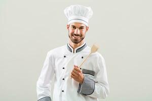 portrait de souriant chef en portant en bois cuillère sur gris Contexte. photo