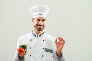 chef est montrant des légumes et D'accord signe sur gris Contexte. photo