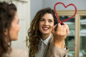 femme d'affaires est dessin cœur avec rouge à lèvres sur le miroir tandis que en train de préparer pour travail photo
