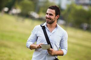 Jeune homme d'affaire est en utilisant numérique tablette à le parc photo