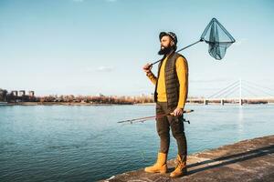 image de pêcheur en portant pêche barre et pêche net tandis que permanent par une rivière photo