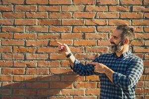 portrait de moderne homme d'affaire avec barbe faire des gestes tandis que permanent dans de face de brique mur Extérieur photo