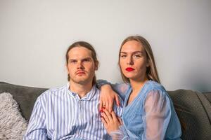 un en colère couple dans lumière bleu vêtements, recroquevillé sur une canapé, regarde devant photo