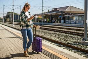 content femme en utilisant mobile téléphone et en portant carte sur une train station photo