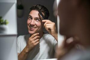 homme ratissage le sien cheveux tandis que à la recherche lui-même dans le miroir photo