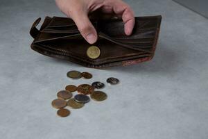 le main de une homme qui est en portant une portefeuille de lequel pièces de monnaie déversé en dehors et un pièce de monnaie dans le portefeuille. sélectif concentrer photo