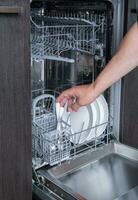 travaux ménagers ouvert le Lave-vaisselle et le la personne met le assiette dans le machine. haute qualité photo