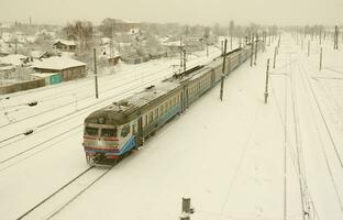 un long train de voitures voyageurs se déplace le long de la voie ferrée. paysage ferroviaire en hiver après les chutes de neige photo