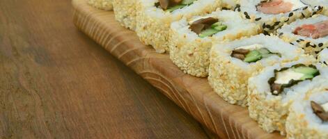 gros plan d'un grand nombre de rouleaux de sushi avec différentes garnitures se trouvent sur une surface en bois. photo macro de plats japonais classiques cuits avec un espace de copie