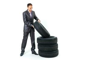 plein longueur portrait de une Jeune homme d'affaire penché sur une pile de voiture pneus isolé sur blanc Contexte photo