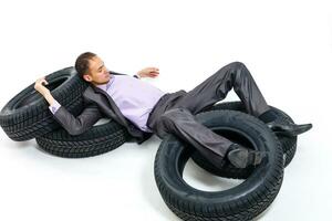 plein longueur portrait de une Jeune homme d'affaire penché sur une pile de voiture pneus isolé sur blanc Contexte photo