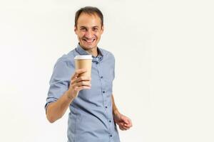 content Jeune homme dans une chemise détient une tasse de café dans le sien mains, regards dans le caméra et sourires, isolé sur une blanc Contexte. photo