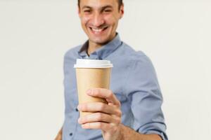 content Jeune homme dans une chemise détient une tasse de café dans le sien mains, regards dans le caméra et sourires, isolé sur une blanc Contexte. photo