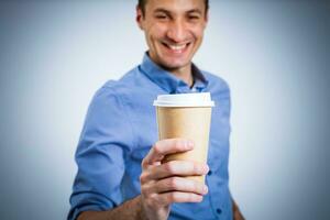 content Jeune homme dans une chemise détient une tasse de café dans le sien mains, regards dans le caméra et sourires, isolé sur une blanc Contexte. photo