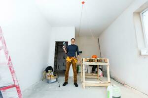 Accueil réparation. Masculin mains en utilisant un électrique perforateur percer avec une percer faire une trou dans le mur avec peeling peindre. photo